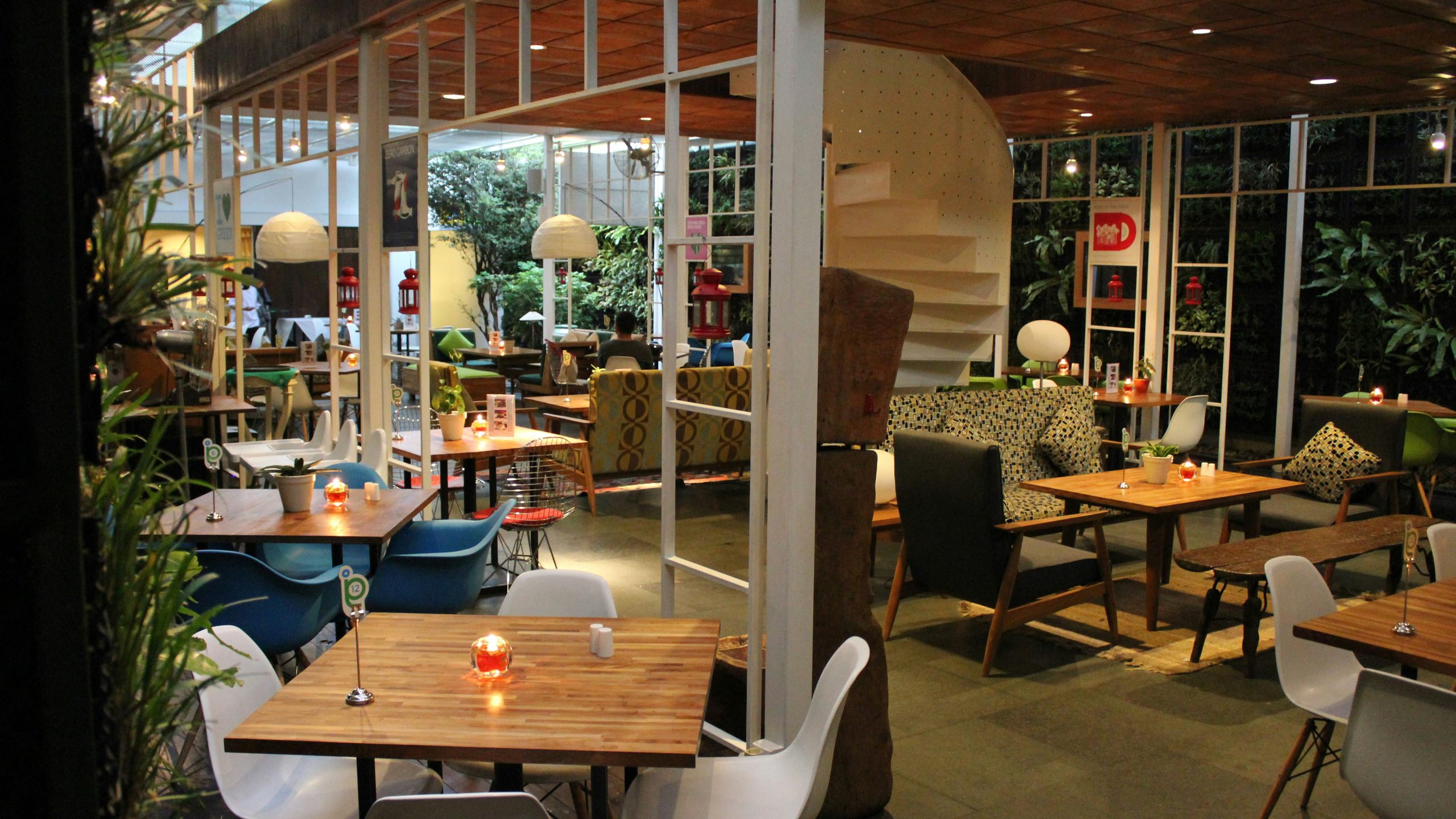 Glasshouse restaurant with white steel frame, plants and light timber tables