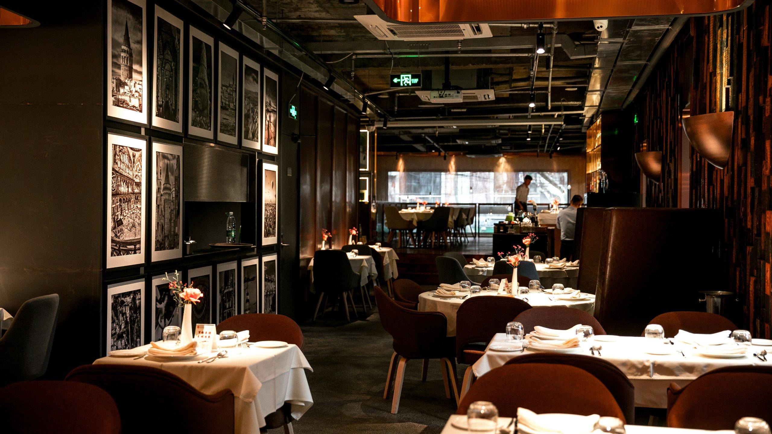 Low-lit fine dining room with photograph wall and white linen round tables