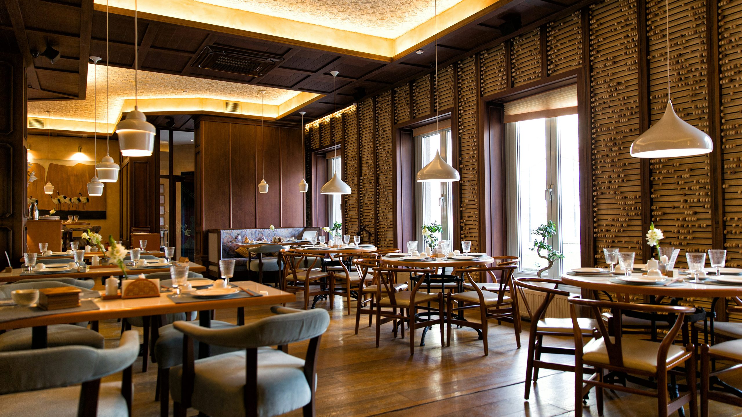 Restaurant dining room with timber slat walls, cove lighting and round timber tables