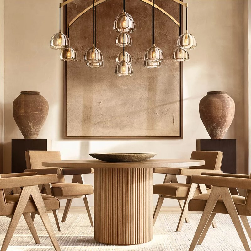 Round oak table with fluted base in a warm dining room with tub chairs and blown-glass pendants